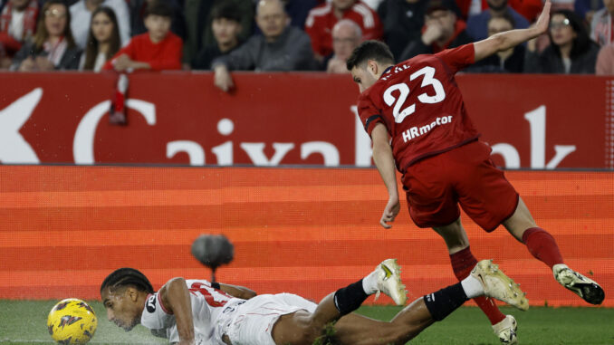 Loïc Badé (i), defensa francés del Sevilla, cae al terreno de juego ante Raúl García, en el estadio Sánchez Pizjuán en foto de archivo de Julio Muñoz. EFE
