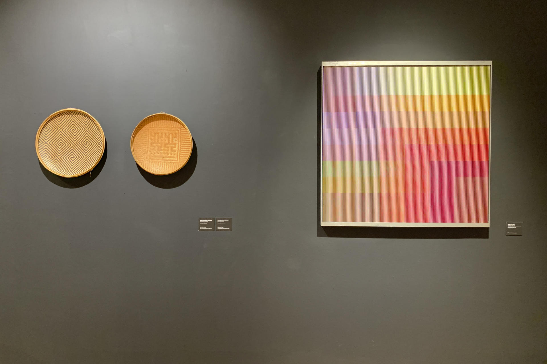 Piezas de cestería ye'kwana de la exposición 'Convergencias/Divergencias' de la Casa de América de Madrid, junto a un cuadro del artista venezolano fallecido Carlos Cruz-Diez. EFE/ Mariana López Alba
