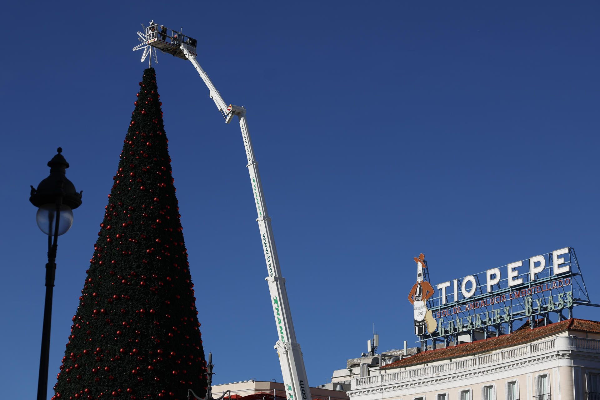 Operarios ponen a punto la estrella que corona el árbol de Navidad en la Puerta del Sol en Madrid, este soleado lunes. EFE/ Mariscal
