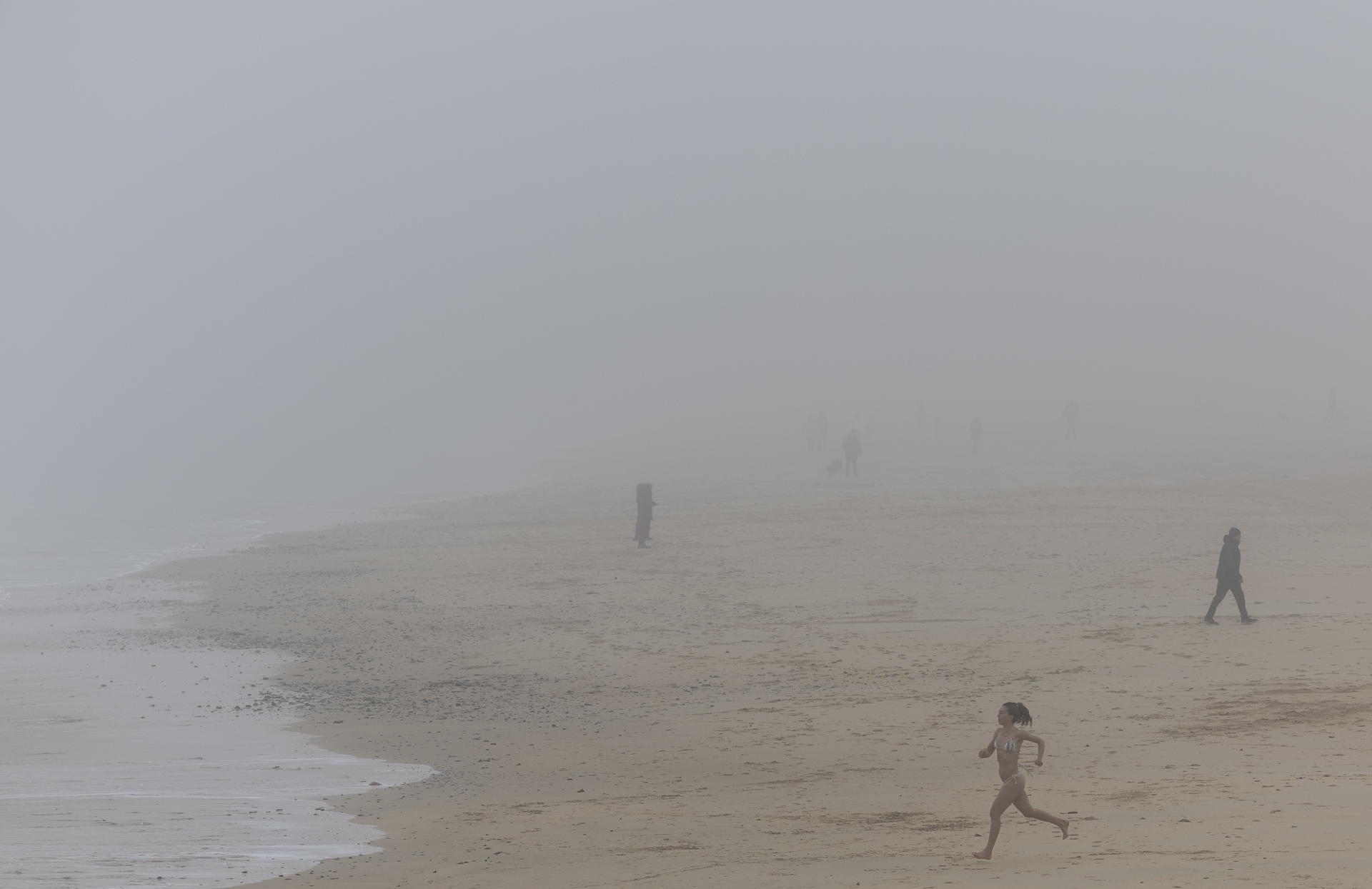 Una mujer corre hacia el agua en la playa de Ondarreta de San Sebastián que este viernes ha amanecido cubierta por una densa niebla. EFE/Juan Herrero.
