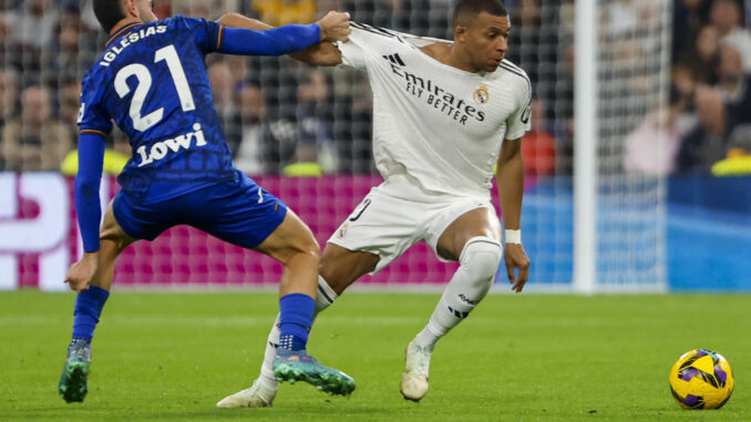 El delantero francés del Real Madrid Kylian Mbappé (d) pelea un balón con el defensa del Getafe Juan Iglesias en el partido de LaLiga entre el Real Madrid y el Getafe, este domingo en el estadio Santiago Bernabéu. EFE/ Sergio Pérez
