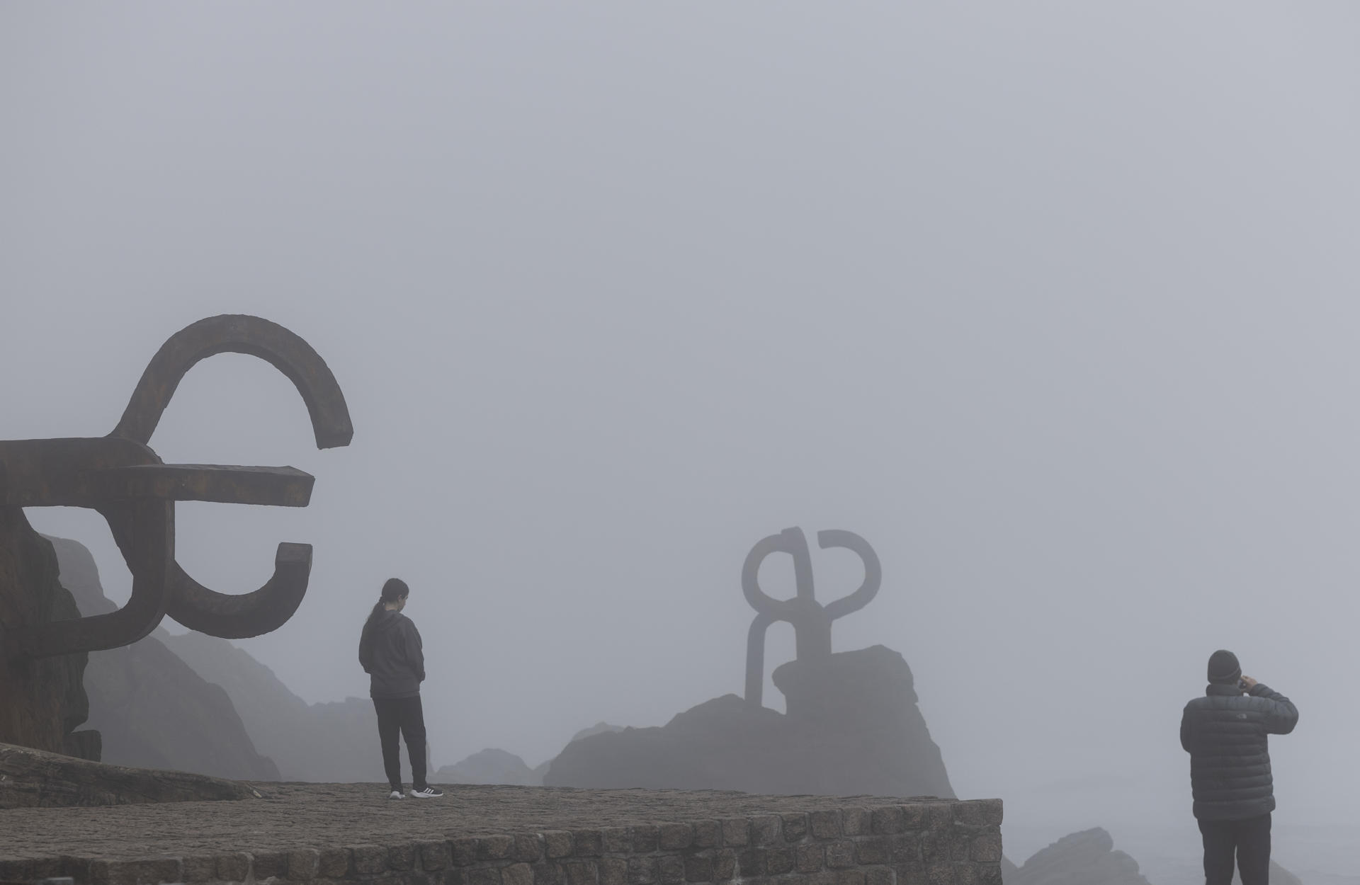 Un hombre fotografía las esculturas del Peine del Viento de San Sebastián que este viernes han amanecido cubiertas por una densa niebla. EFE/Juan Herrero.
