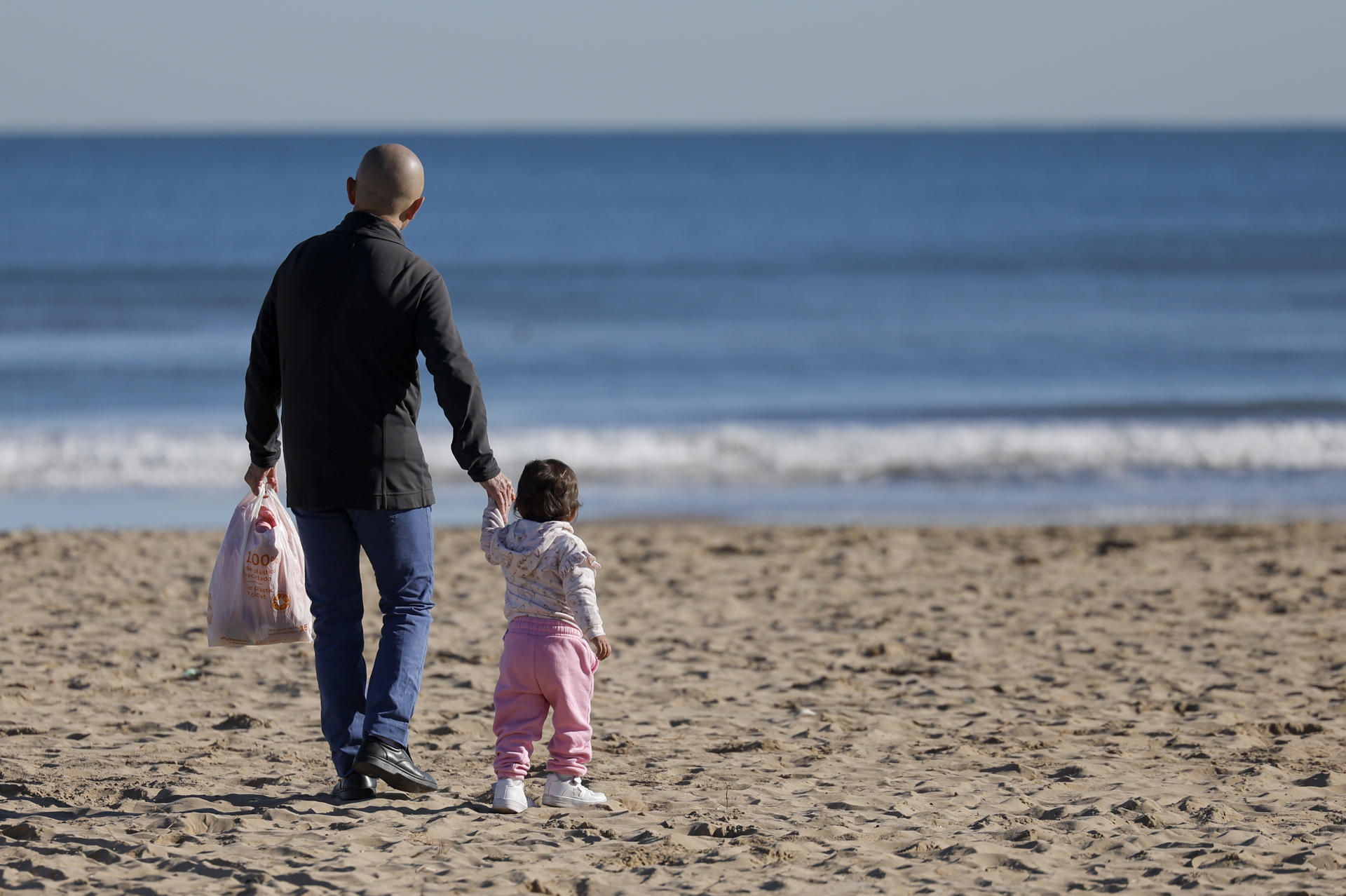 Un hombre pasea por la playa de la Malavarrosa con una niña. EFE/Kai Försterling
