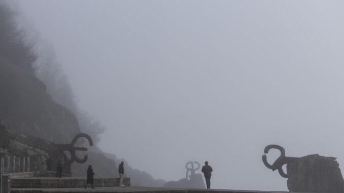 Paseantes caminan entre las esculturas del Peine del Viento de San Sebastián que este viernes han amanecido cubiertas por una densa niebla. EFE/Juan Herrero.
