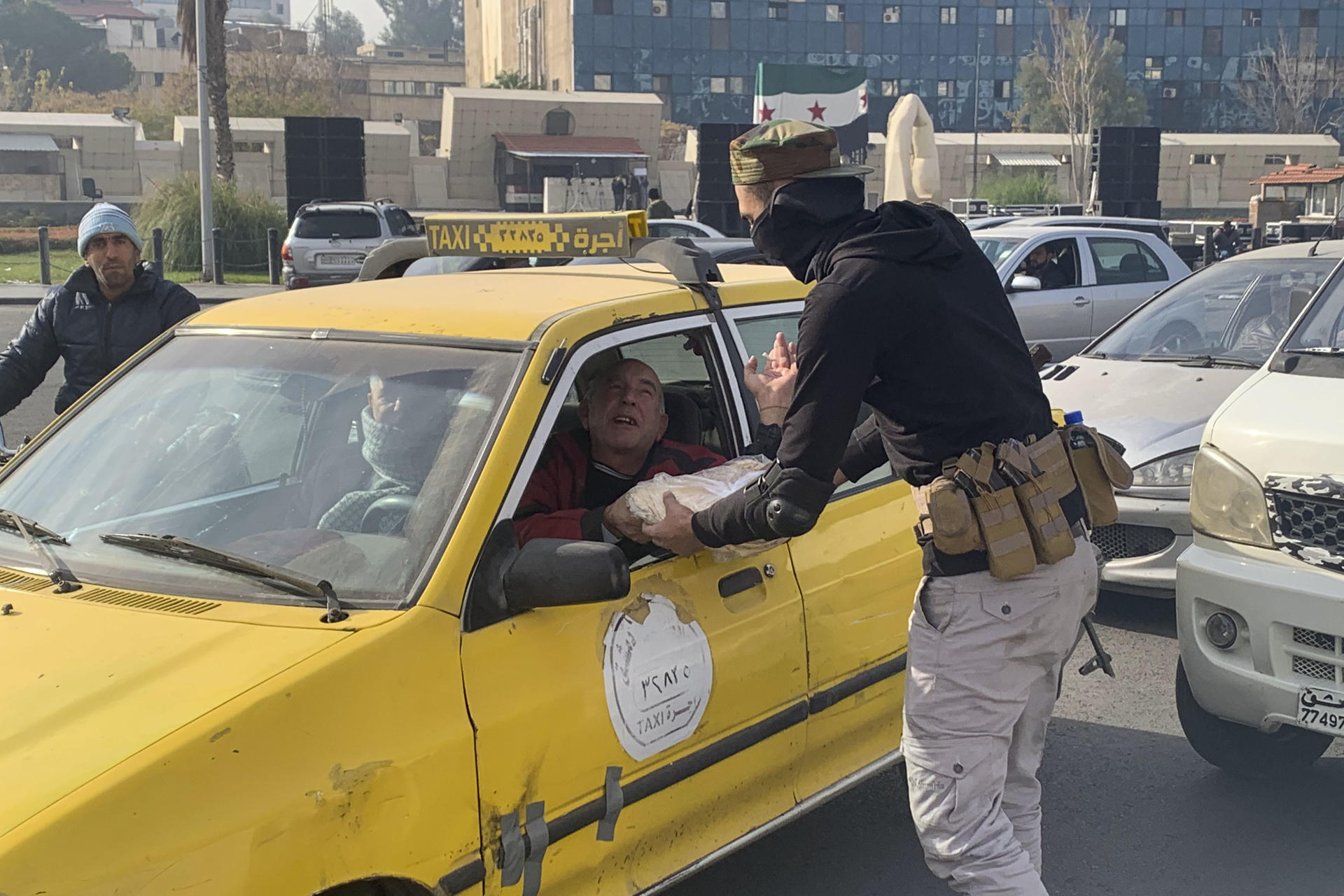 Un hombre armado entrega comida a un taxista este jueves en la Plaza de los Omeyas en Damasco, ciudad que vive unos días de transición tras la reciente caída del régimen de Bachar al Asad. EFE/Álvaro Mellizo
