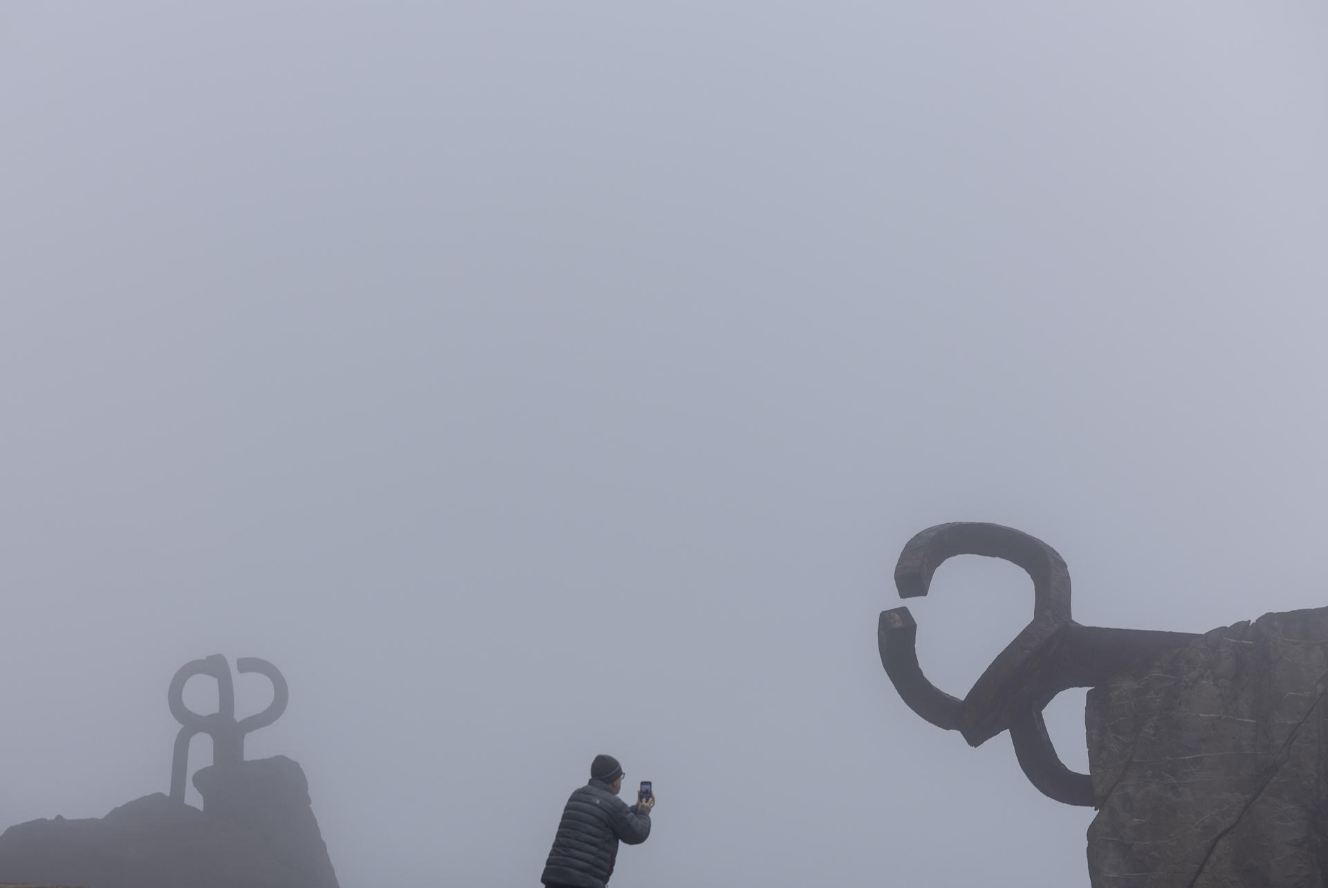 Un hombre fotografía las esculturas del Peine del Viento de San Sebastián que este viernes han amanecido cubiertas por una densa niebla. EFE/Juan Herrero.
