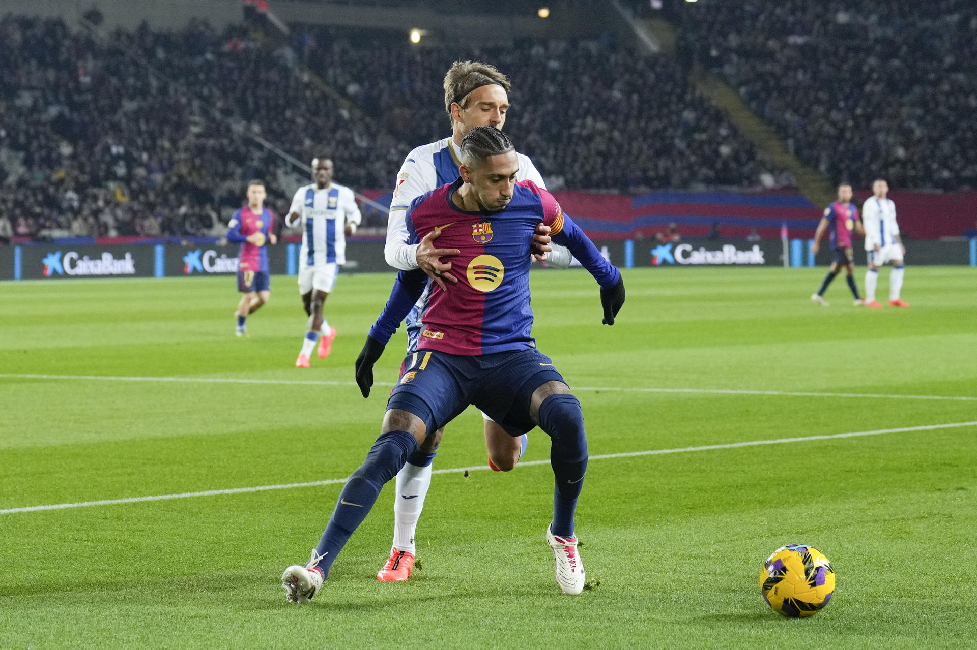 El delantero del FC Barcelona Raphinha (delante) lucha con Sergio González, del Leganés, durante el partido de la jornada 17 de LaLiga que FC Barcelona y CD Leganés disputan este domingo en el estadio Lluís Companys, en Barcelona. EFE/Alejandro García
