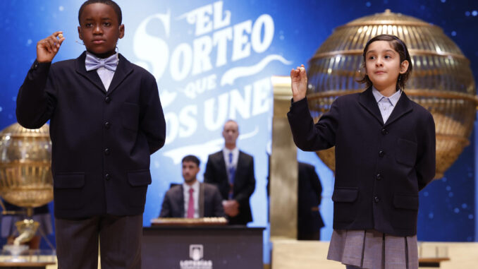 Los niños de la Residencia San Ildefonso de Madrid Ángel Abaga Elebiyo (i) y Aurora Rodríguez Ososrio (d) muestran el número 72.853, uno de los quintos premios, durante el sorteo de la Lotería de Navidad que se celebra este domingo en el Teatro Real, en Madrid. EFE/Javier Lizón
