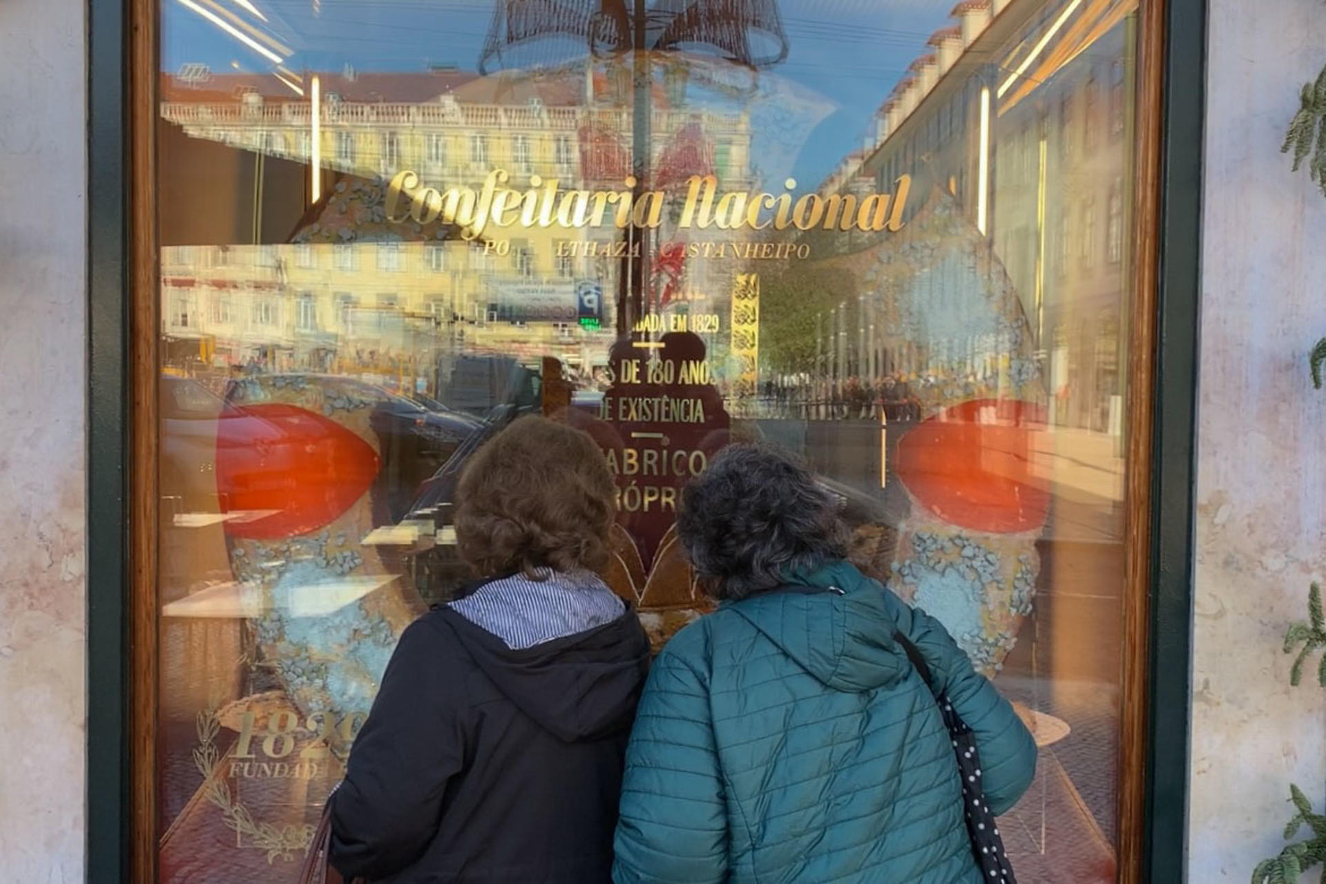 Dos mujeres observan este viernes, los 'bolos rei' expuestos en el escaparate de la Confeitaria Nacional de Lisboa. El obrador de Lisboa que presume de inventar este bizcocho circular con azúcar y fruta escarchada: todo un clásico de la Navidad en Portugal desde su invención a finales del siglo XIX. EFE/ Carlos Caselles
