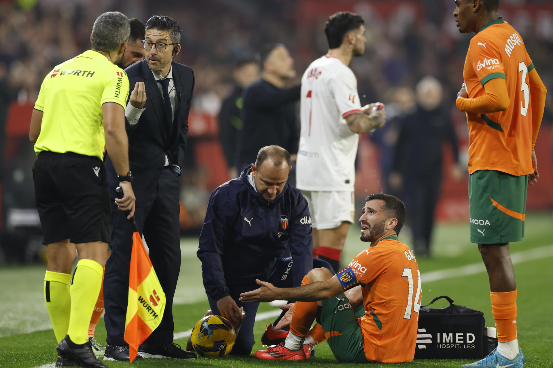 El defensa del Valencia José Gayá (2d) recibe asistencia médica durante el partido de la jornada 19 de LaLiga que Sevilla FC y Valencia CF disputan este sábado en el Ramón Sánchez-Pizjuán, en Sevilla. EFE/Julio Muñoz
