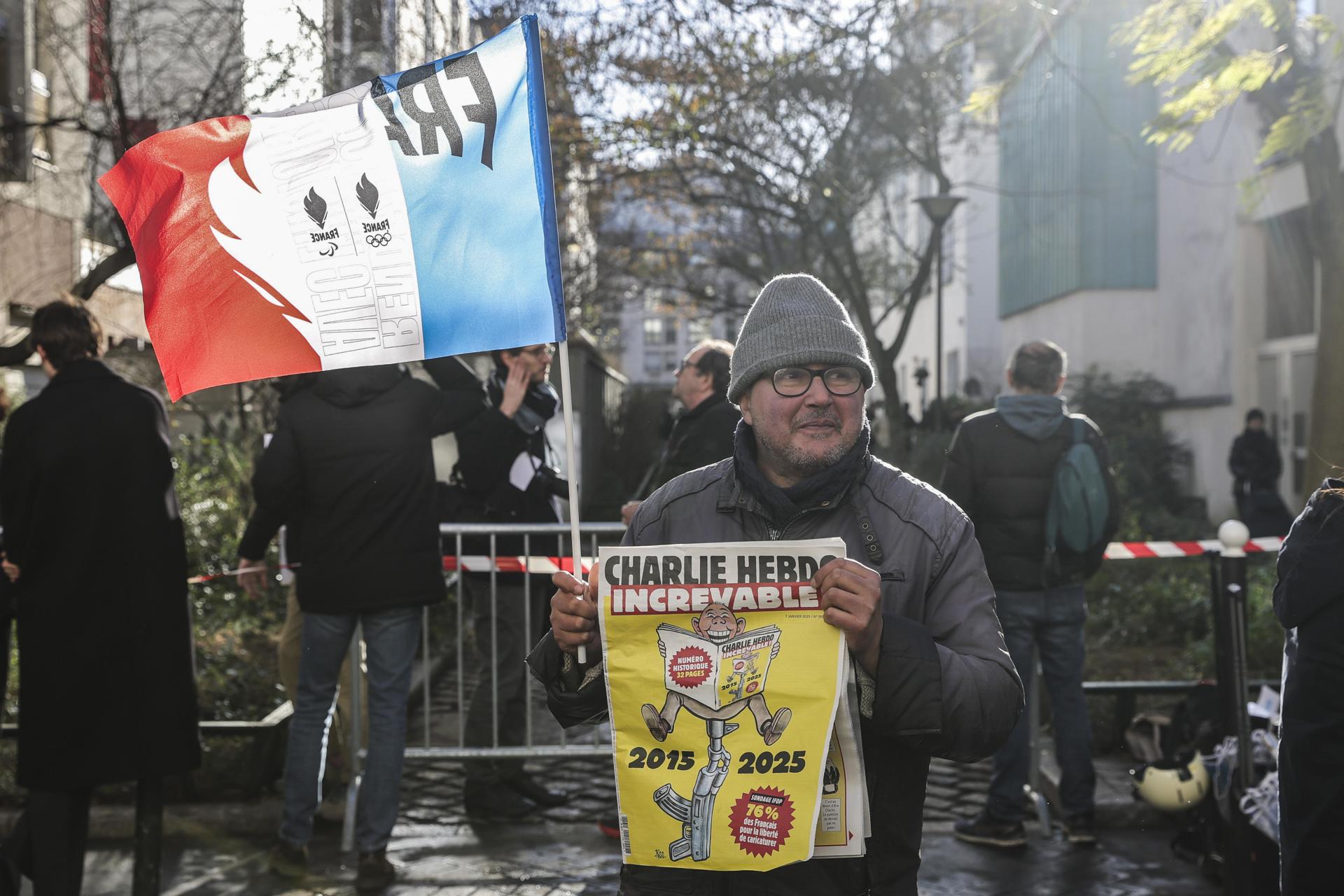 Un hombre sostiene una bandera francesa y el último número de la revista satírica francesa Charlie Hebdo afuera de las antiguas oficinas de la revista, en el décimo aniversario del ataque terrorista en París, Francia.EFE/EPA/Teresa Suarez
