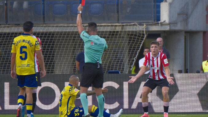 El árbitro Miguel Ángel Ortiz Arias, que dirigirá la semifinal de la Supercopa entre el Athletic y el Barcelona, en el momento de sacar tarjeta roja a Mikel Jauregizar (d), durante el encuentro de la quinta jornada de LaLiga ante la UD Las Palmas. EFE/Ángel Medina G.
