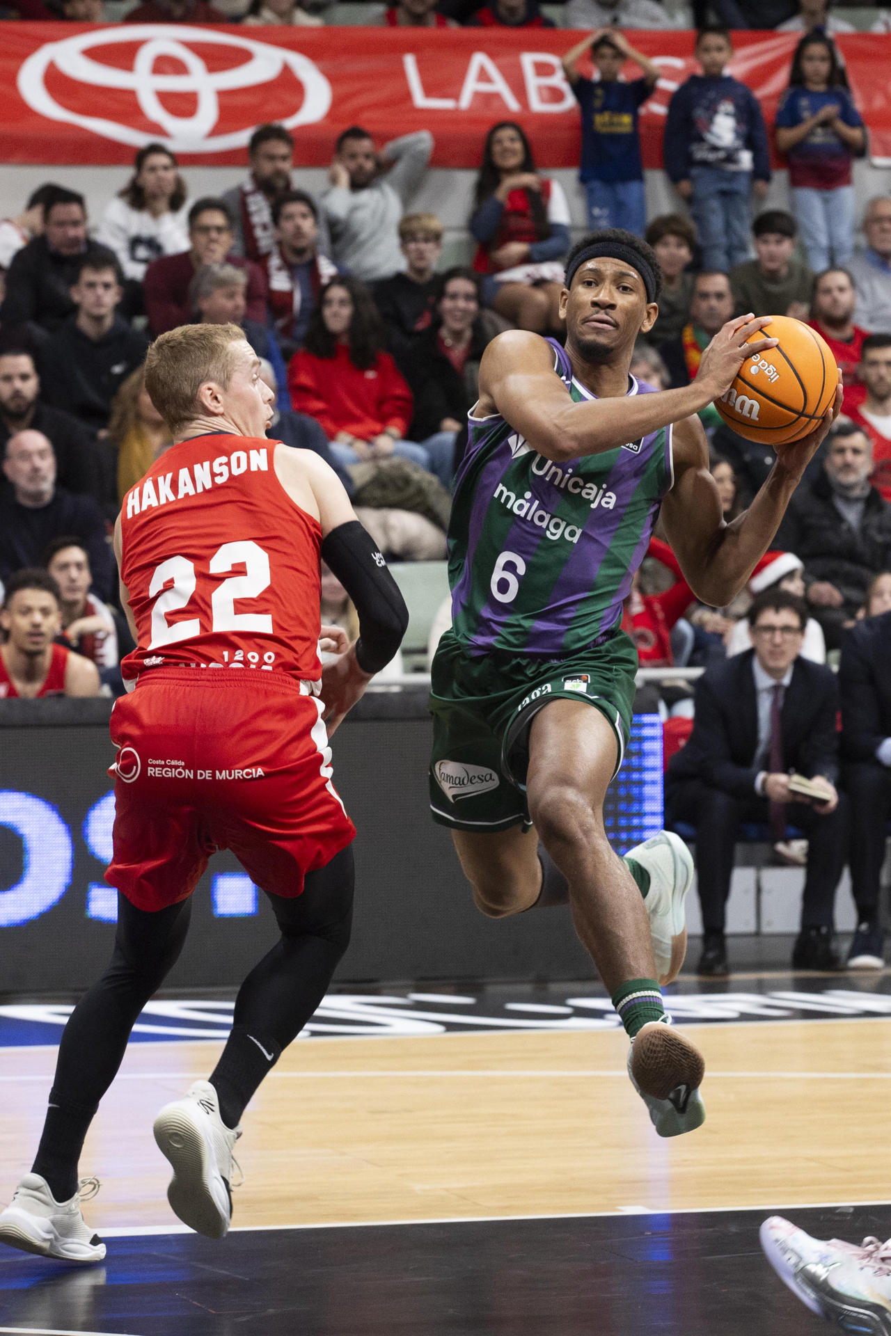 El escolta estadounidense de Unicaja Kameron Taylor (d) controla el balón ante el base sueco de UCAM Murcia Ludde Hakanson (i), durante el partido de la décimo cuarta jornada de la liga Endesa que están disputando este jueves en el Palacio de los Deportes de Murcia. EFE/Marcial Guillén
