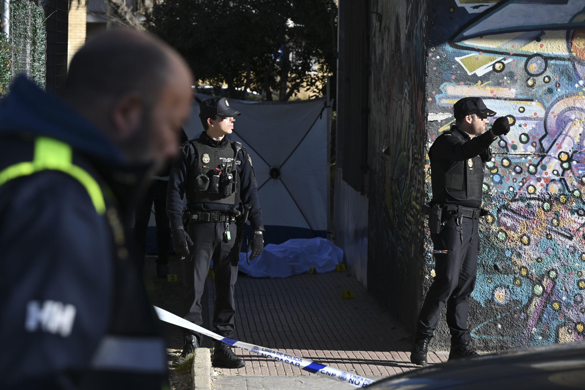 Agentes de la Policía Nacional junto al cuerpo de un hombre de unos 60 años, que ha aparecido muerto en la mañana de este lunes con heridas de arma de fuego en la localidad madrileña de Alcalá de Henares. EFE/ Fernando Villar
