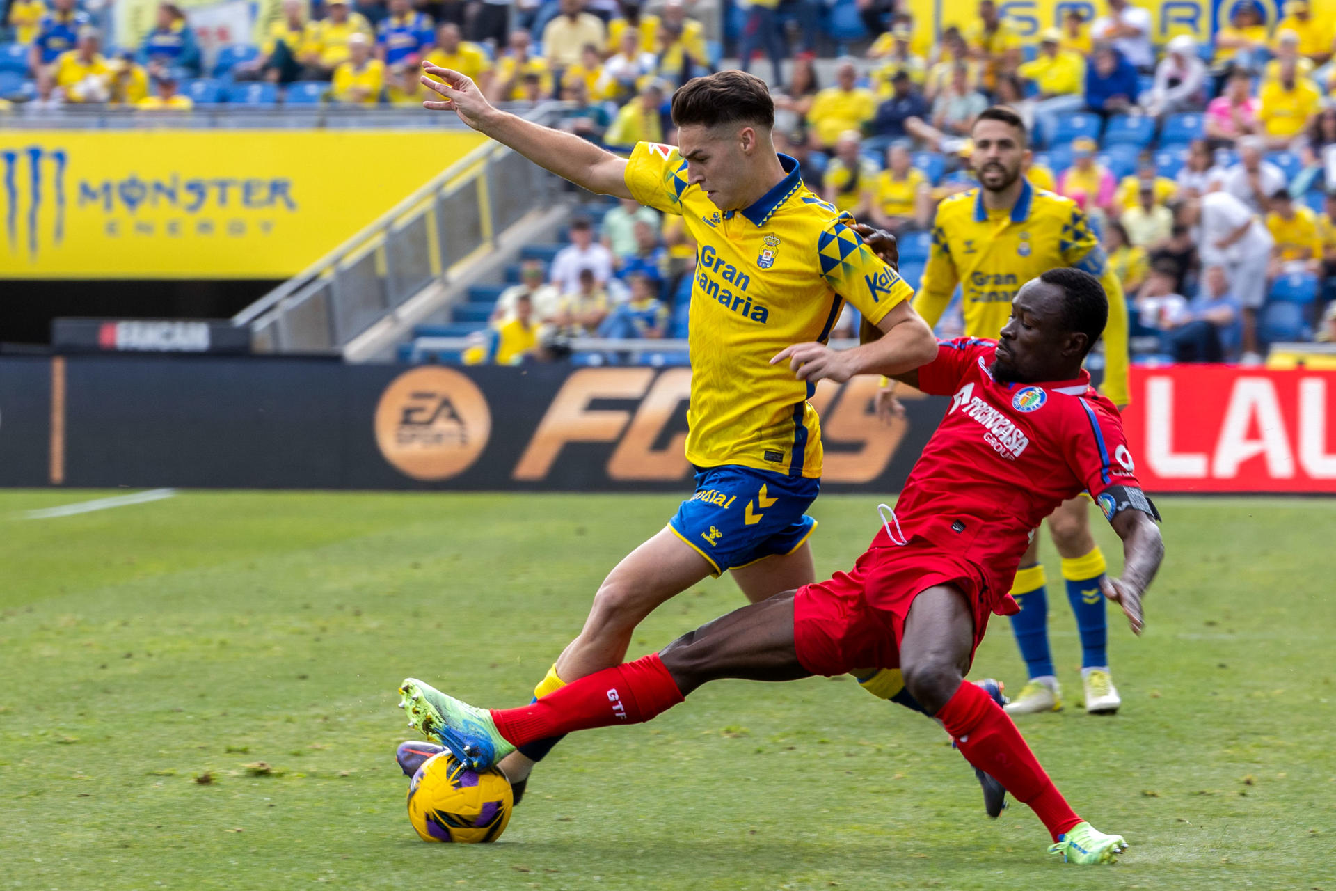 El defensa de la UD Las Palmas, Mika Mármol (i) lucha por el balón con el defensa Djené Dakonam (d) del Getafe durante el partido correspondiente a la jornada 19 de LaLiga disputado este domingo en el estadio de Gran Canaria. EFE/ Quique Curbelo
