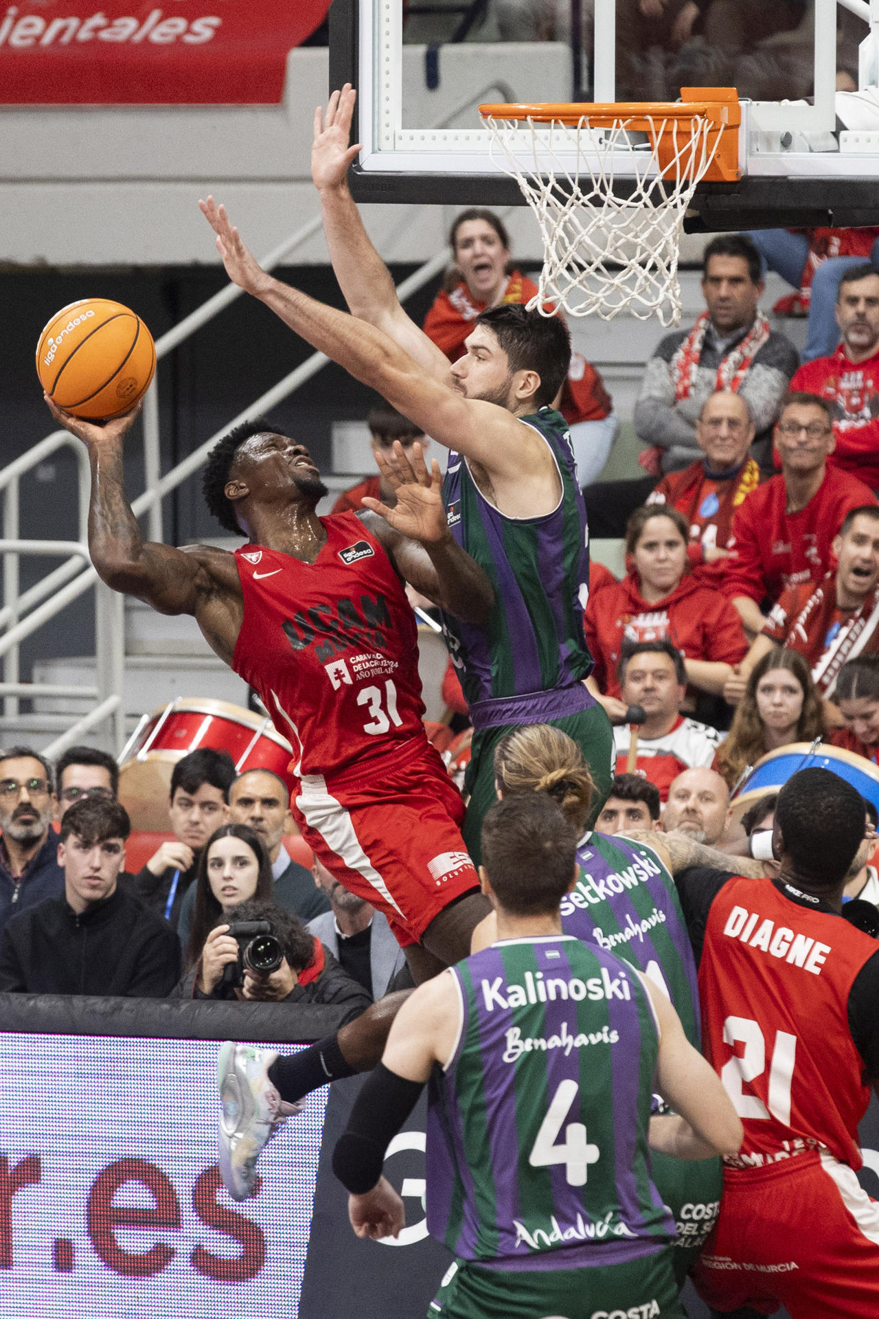 El base estadounidense de UCAM Murcia Dylan Ennis (i) intenta encestar ante la presión del pívot de Unicaja Málaga David Kravish (d) durante el partido de la décimo cuarta jornada de la liga Endesa que UCAM Murcia y Unicaja Málaga están disputando este jueves en el Palacio de los Deportes de Murcia. EFE/Marcial Guillén
