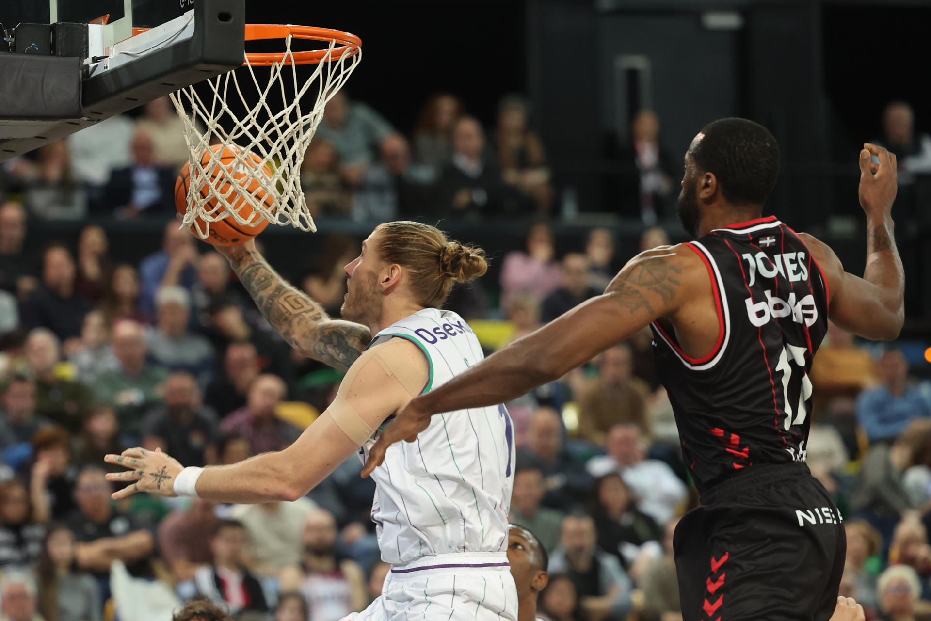 El ala-pívot del Unicaja Dylan Osetkowski (i) entra a canasta perseguido por Marvin Jones, del Bilbao Basket, en el partido de Liga Endesa entre el Bilbao Basket y el Unicaja Málaga que se disputó en el Bilbao Arena. EFE/ Luis Tejido
