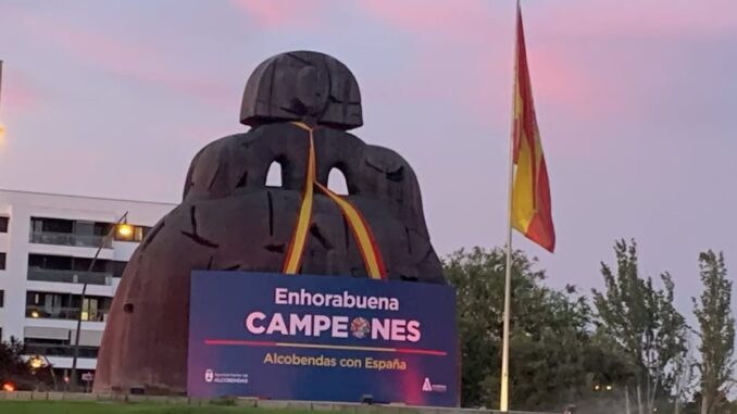 Collage con tres imágenes de Alcobendas celebrando: La Menina con bufanda roja, cascada iluminada en rojo y amarillo, y fachada del Ayuntamiento con lona que dice Enhorabuena Campeones