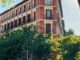 Fachada de edificio clásico en la Calle de Alcalá de Madrid con arquitectura de ladrillo rojo, árboles y actividad urbana