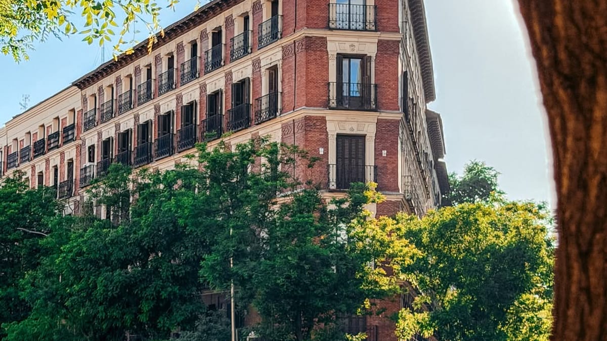 Fachada de edificio clásico en la Calle de Alcalá de Madrid con arquitectura de ladrillo rojo, árboles y actividad urbana
