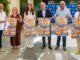 IV Feria del Marisco y la Gastronomía de Isla Cristina con personas sosteniendo carteles de promoción del evento