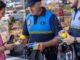Tres personas en un entorno exterior con agentes de seguridad municipal y una mujer en vestido rosa