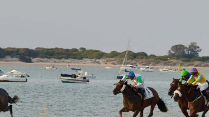 Competición de carreras de caballos en la playa de Sanlúcar de Barrameda con jinetes disputando una carrera sobre arena mojada frente al mar