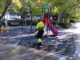 Trabajador municipal con chaleco amarillo fluorescente realizando limpieza con agua a presión en un área infantil de un parque de Cuenca