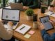 Reunión de trabajo en oficina con profesionales alrededor de mesa con laptops y dispositivos tecnológicos