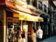 Vista urbana de Madrid mostrando espacios comerciales y callejeros con tiendas como Carrefour Express y La Gramola, capturada con efecto de grano cinematográfico