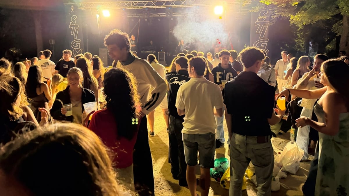 Escena nocturna de la verbena en el Parque de Santa Ana de Cuenca con cientos de personas reunidas, iluminación de escenario y árboles decorados