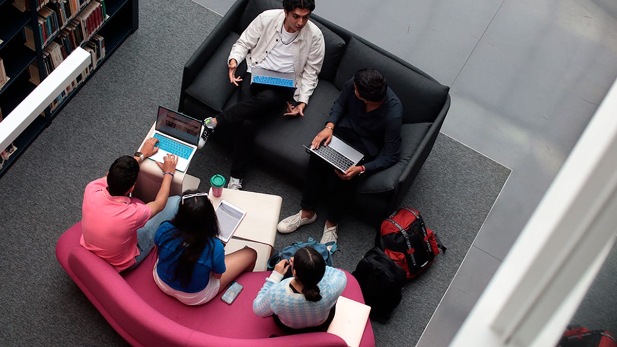 Grupo de estudiantes en espacio de trabajo colaborativo con sofás y laptops en la universidad
