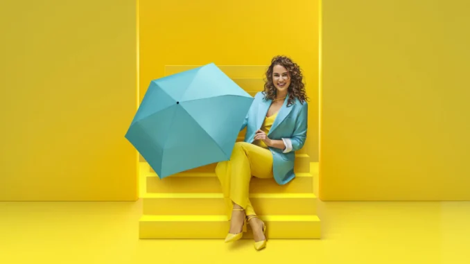 Mujer sonriente paraguas azul celeste Mujer con chaqueta azul sentada en escaleras amarillas sosteniendo un paraguas celeste abierto.