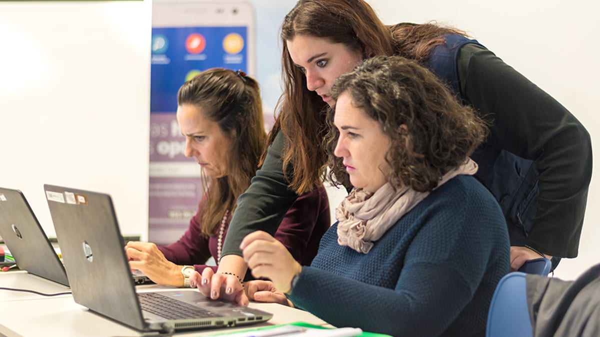 Tres mujeres trabajando colaborativamente frente a laptops en un entorno de oficina, representando capacitación y transformación digital