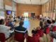 Reunión del Consejo Sectorial de Personas Mayores de Cáceres con participantes sentados en sillas rojas durante la aprobación de ayudas a asociaciones