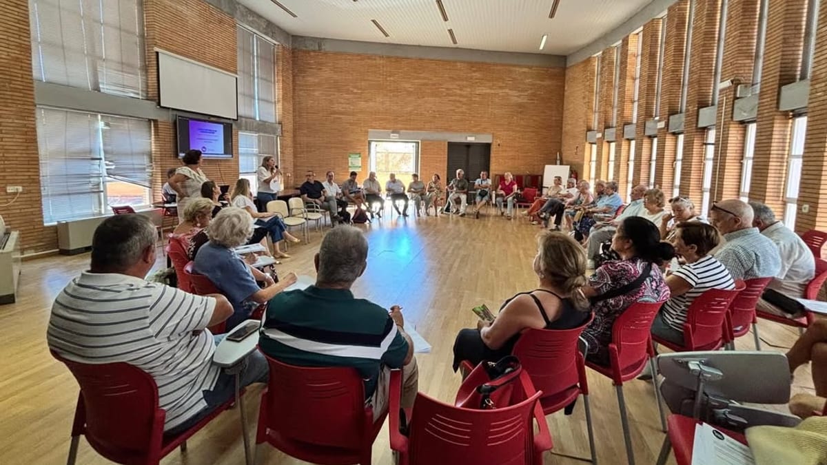 Reunión del Consejo Sectorial de Personas Mayores de Cáceres con participantes sentados en sillas rojas durante la aprobación de ayudas a asociaciones