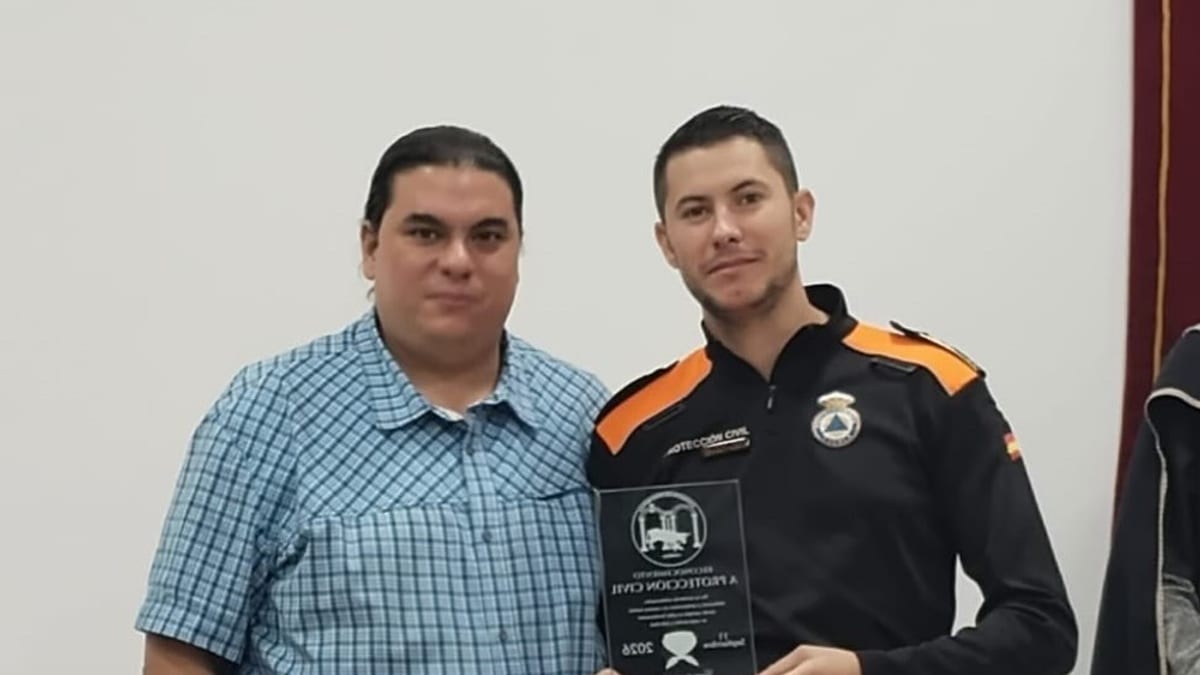 Dos personas posando juntas, una de ellas sostiene una placa de reconocimiento