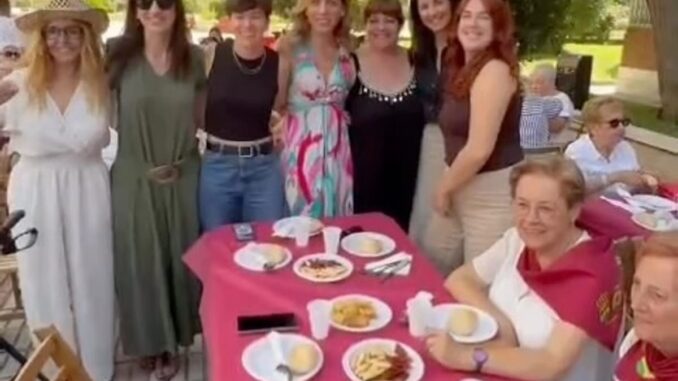 Celebra la XLVII edición del Día de la Mujer en Parque Grande en Alcorcón Reunión festiva al aire libre en la Asociación Parque Grande durante la celebración del Día de la Mujer en Alcorcón, con asistentes, mesa decorada con mantel rosa, comida y bebidas, e instalaciones decorativas con cintas de colores